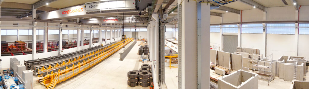 Produktionshalle mit automatisierter Fertigungsanlage, Kranbahn und gelagerten Stahlbauteilen.