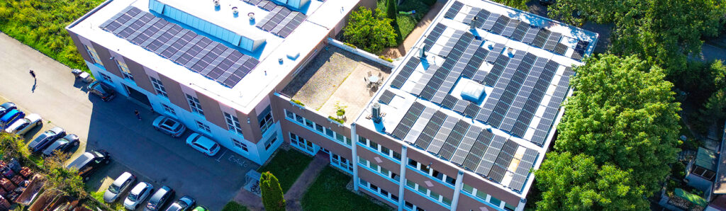 Luftaufnahme eines Industrie‑ und Bürogebäudes mit großflächigen Photovoltaikanlagen