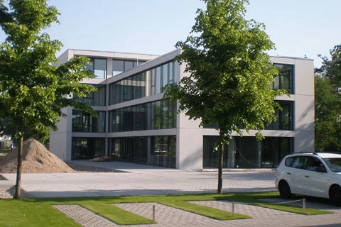 Modernes Verwaltungs- oder Bürogebäude mit großen Fensterflächen und Bäumen im Vordergrund.