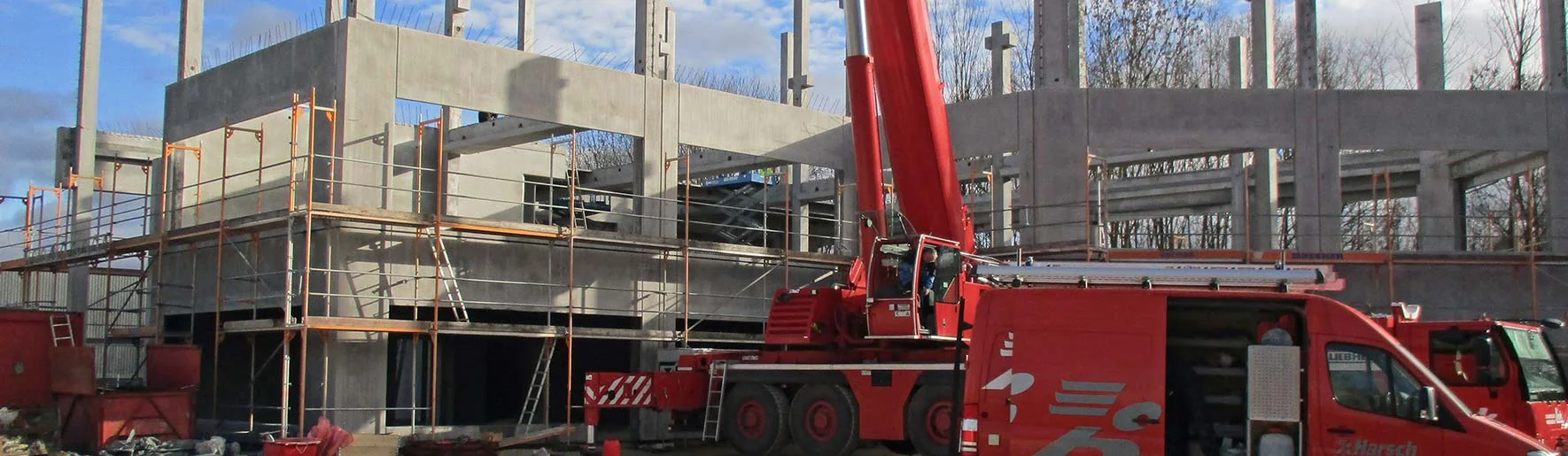 Mehrgeschossiger Betonrohbau mit umlaufendem Gerüst, Betonfertigteilen und Mobilkran im Einsatz