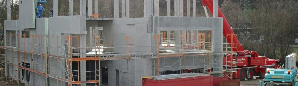 Mehrgeschossiger Betonrohbau mit montierten Fertigteilelementen, umlaufendem Gerüst und Kranarbeiten