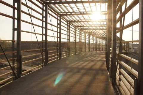 Stahlkonstruktion eines überdachten Gangs im Bau mit einfallendem Sonnenlicht.