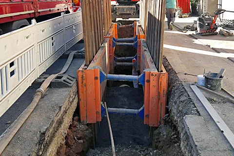 Offener Kanalgraben mit Verbausystem und verlegten Rohrleitungen im Straßenraum.