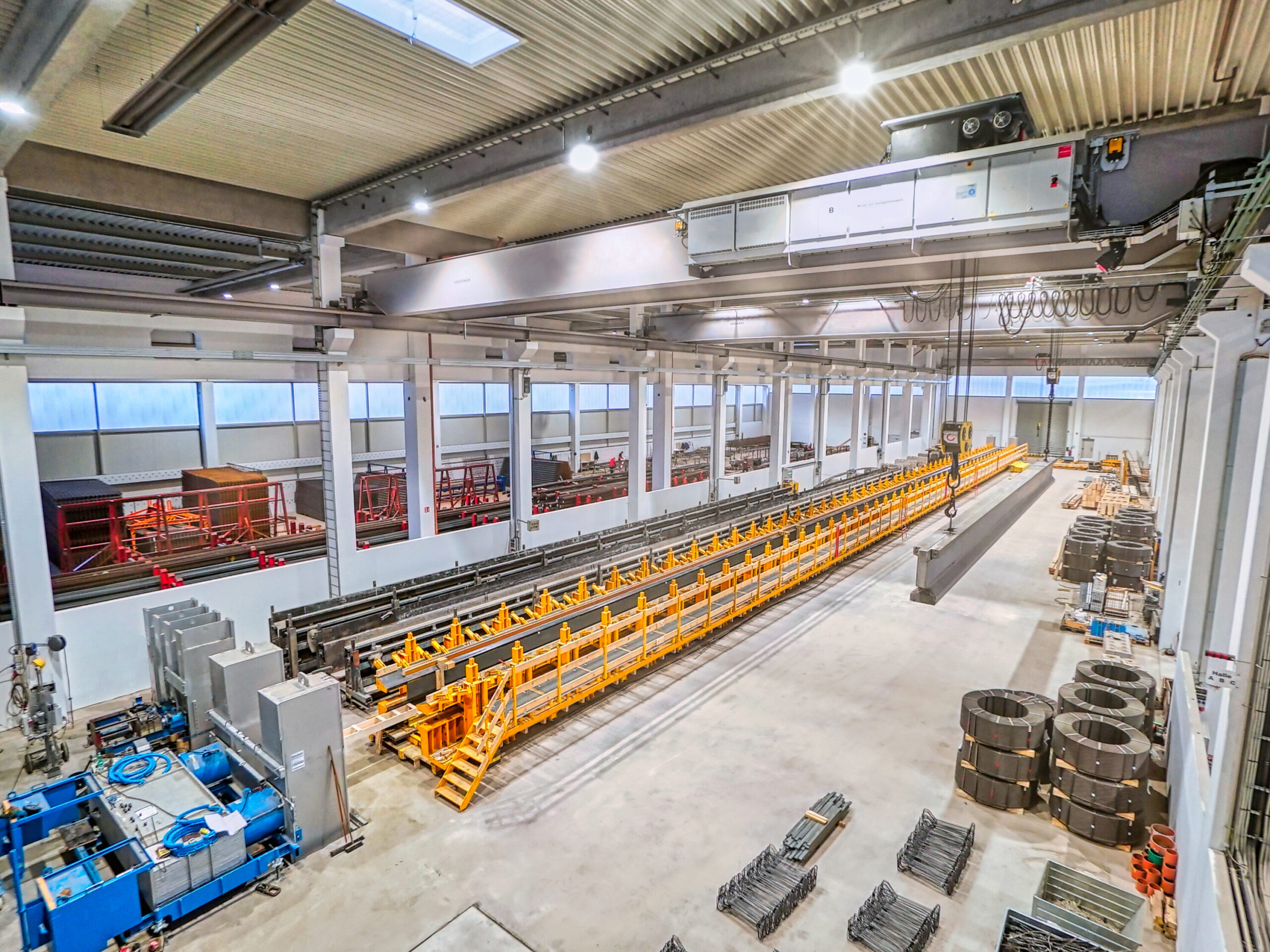 Produktionshalle mit automatisierter Fertigungsanlage, Kranbahn und gelagerten Stahlbauteilen.